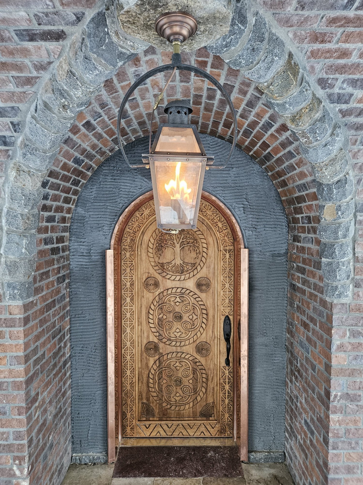 Hand-carved wood door beneath a brick archway, lit by a custom gas lantern
