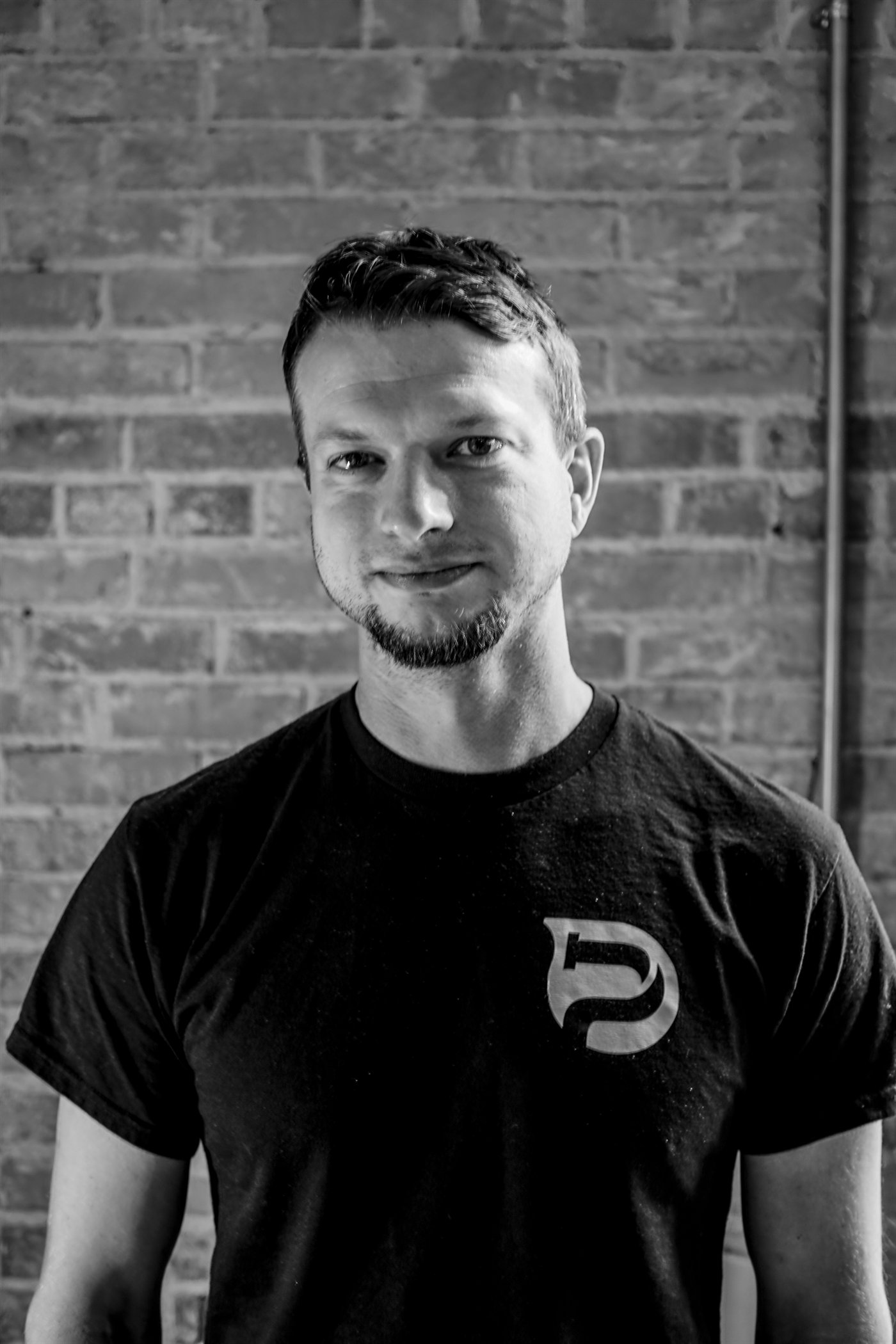 Tyler Bethke, owner of Plumbellum, portrait in a Plumbellum t-shirt against a brick wall